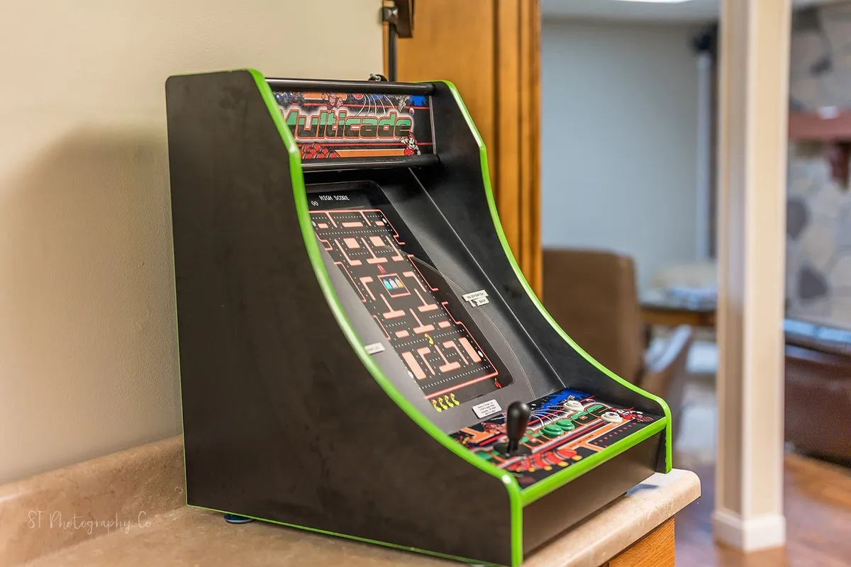 A classic arcade machine stands ready for action, set against a neutral interior wall. The setup is nostalgic and playful, evoking fond memories of arcade nights and friendly high-score battles.