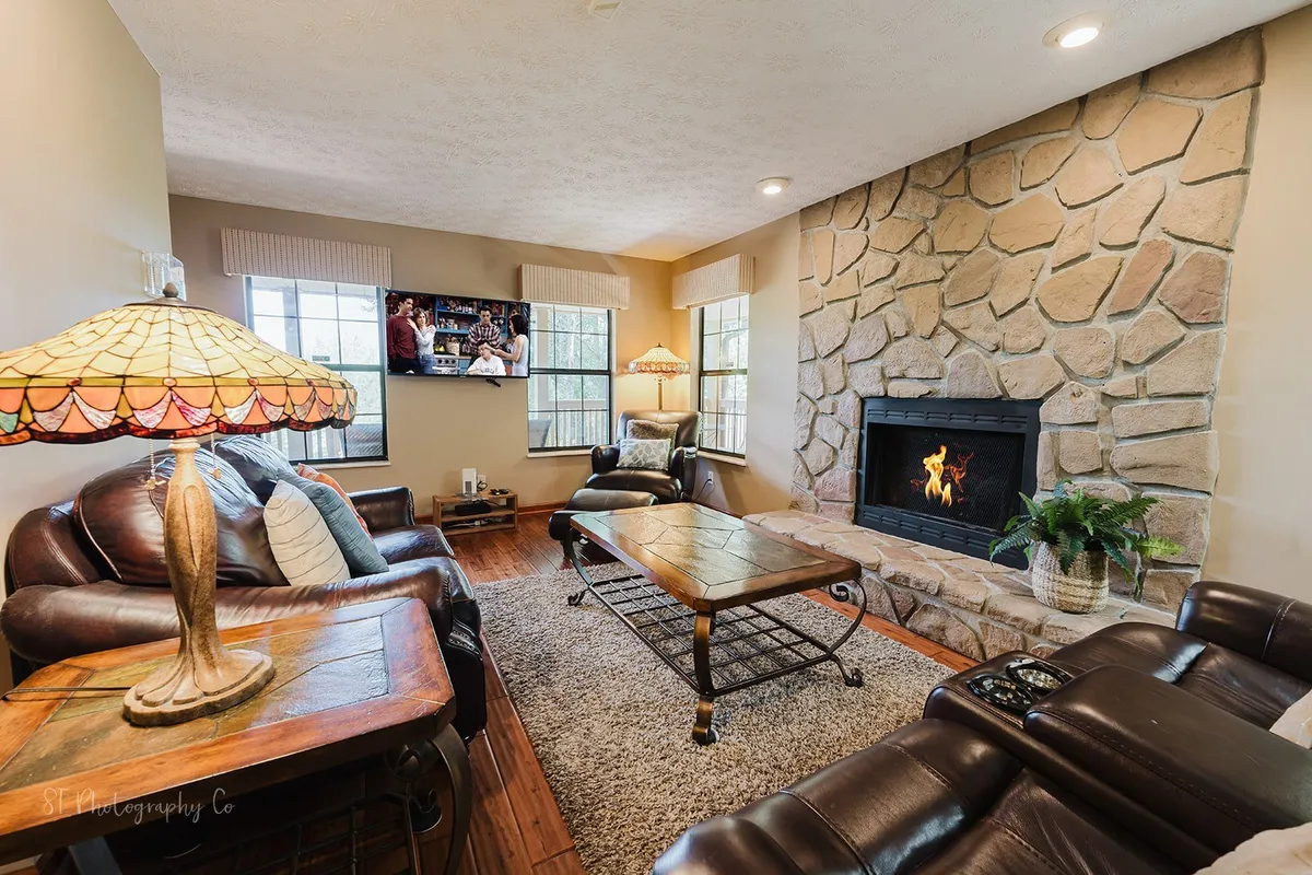 A warm living area with a stone fireplace, plush leather sofas, a central coffee table, and soft ambient lighting from a lamp. The space is inviting and ideal for cozy movie nights, story sharing, or simply relaxing with loved ones.