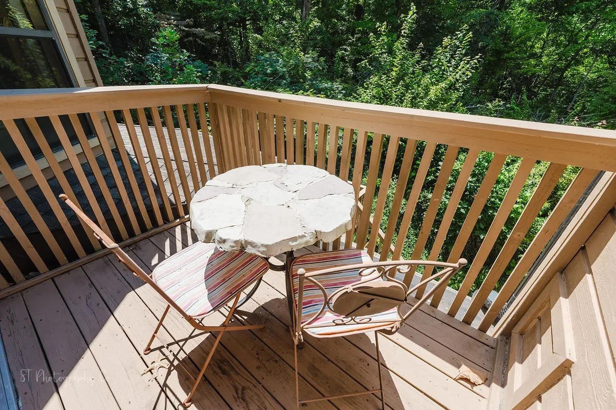 A cozy outdoor seating area on a balcony, featuring a stone table and striped chairs, with a wooden railing and vibrant greenery in the background. The scene captures peaceful moments like morning coffee or evening stargazing amid the scenic landscape.