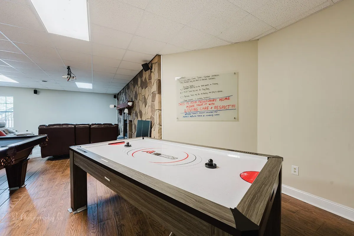 A vibrant interior game room with an air hockey table, comfortable leather couches, and a decorative stone wall. A playful written message on the wall adds character and invites family fun nights spent playing games and relaxing together.
