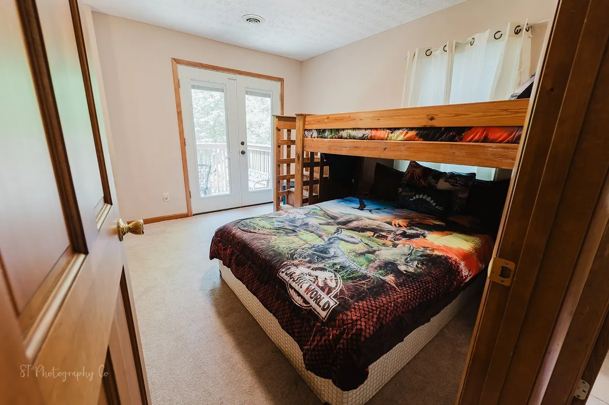 A fun and inviting bunk room with a bunk bed dressed in dinosaur-themed bedding, double doors leading outside, and plenty of sunlight. The space is playful and perfectly suited for children or teens.