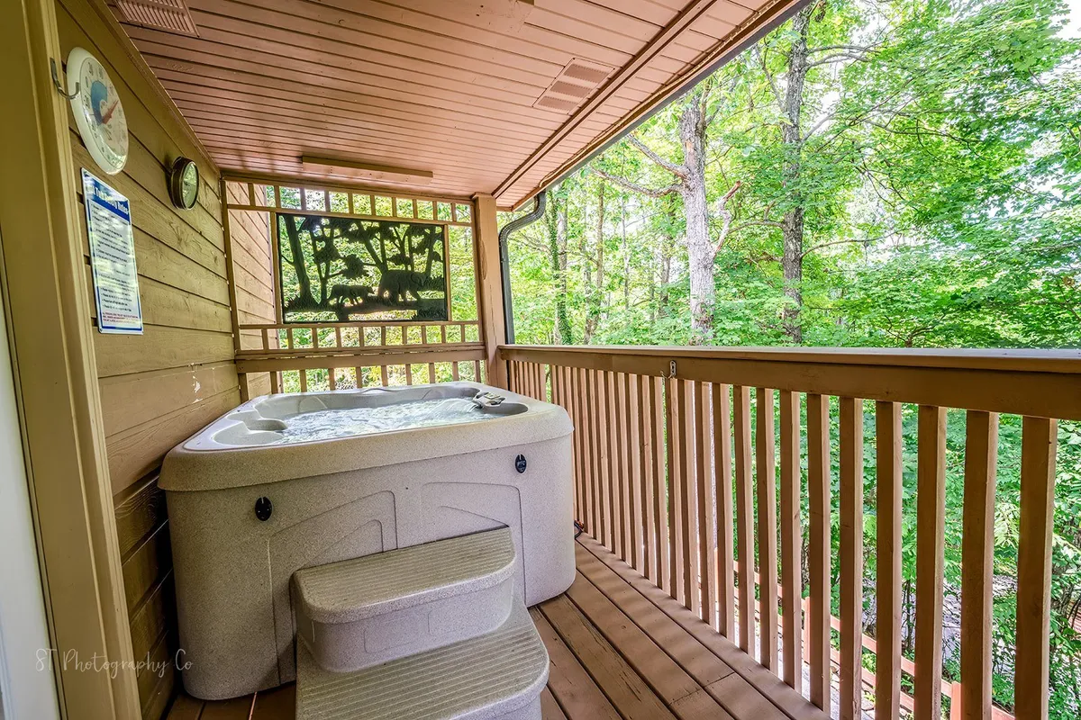 An inviting wooden deck surrounded by lush greenery, featuring a relaxing hot tub with plenty of space for family or friends to gather and unwind together. The tranquil setting highlights the natural beauty of the Smoky Mountains and offers a glimpse into outdoor amenities available at the chalet.