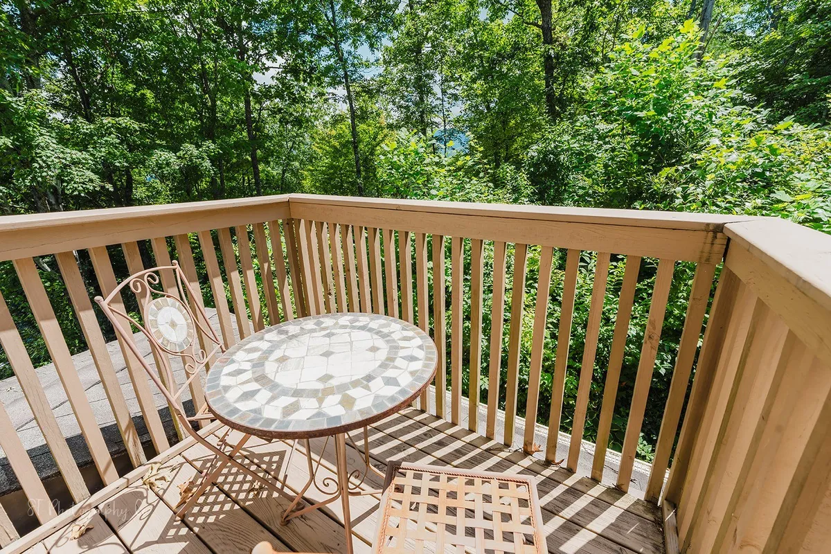 An exterior seating area featuring a decorative table and a metal chair, surrounded by lush greenery. The setup suggests a tranquil spot to enjoy morning coffee or unwind with a book while soaking in the natural scenery.