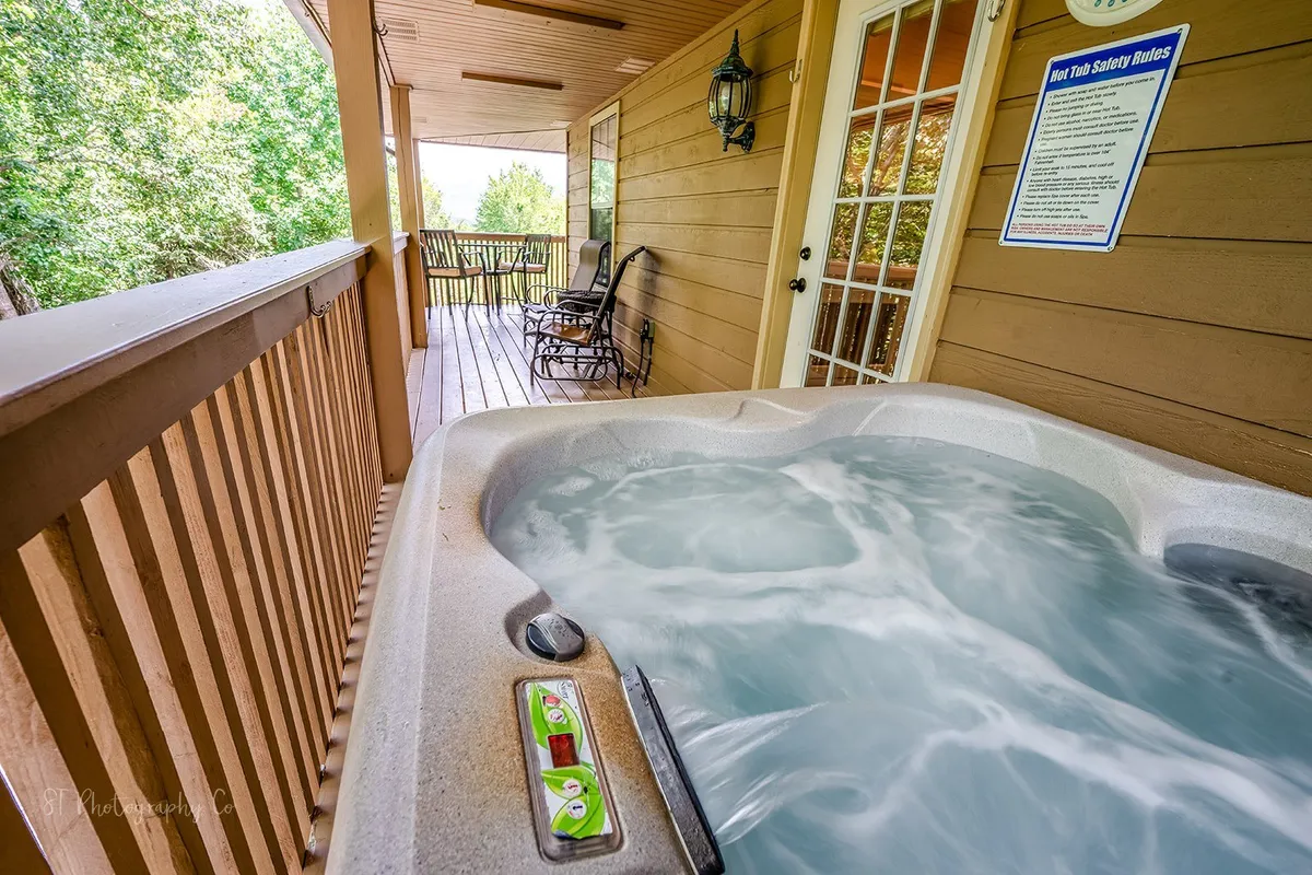 A spacious outdoor deck featuring a hot tub and several rocking chairs, set against a backdrop of natural greenery. The deck offers ample space for socializing, relaxing, and enjoying scenic views, making it ideal for group gatherings or unwinding after a day out.