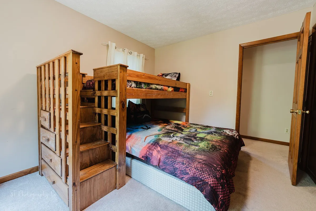 A bunk bed with a vibrant, playful bedspread stands next to a wooden staircase, suggesting a fun sleepover or late-night hangout. The colors and layout feel inviting for children or families seeking a comfortable rest right next to the action.